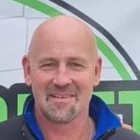 grant-lightfoot A professional man smiling outdoors, wearing a blue jacket, with eco-friendly branding logo in the background.