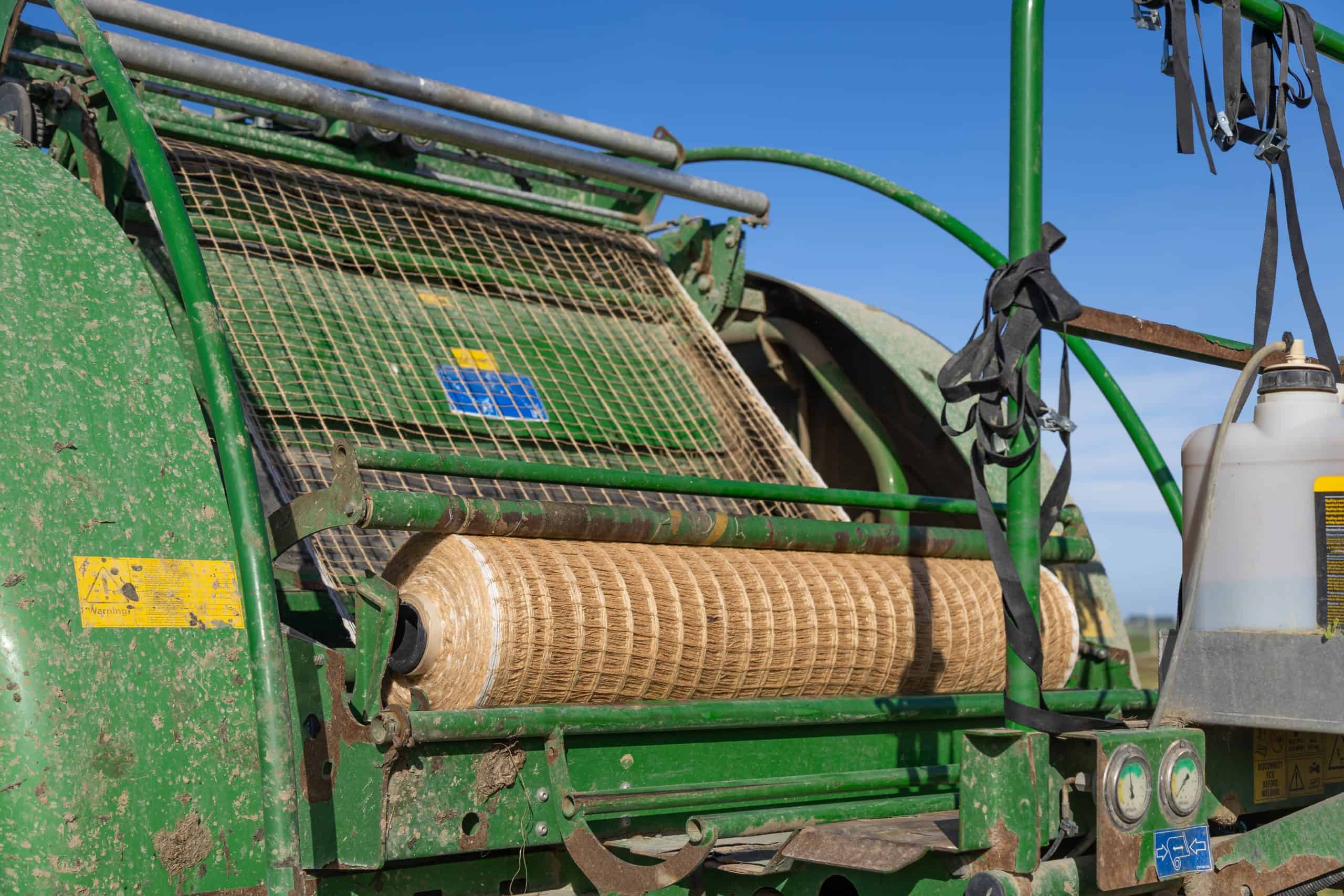 Agricultural machinery with green metal components and a large roller, used for farming or soil preparation, set against a clear blue sky.